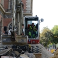 Auf dem Bild ist ein Kran- und Baumaschinenführer zu sehen, der einen Bagger auf einer Baustelle bedient.