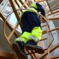 Ein Kranführer in Arbeitskleidung klettert eine Leiter auf einer Baustelle zum Kran hinauf.