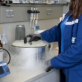 Auf dem Bild ist eine Labortechnikerin zu sehen, die mit einer Apparatur arbeitet, aus der Dampf entweicht.