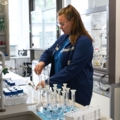 Auf dem Bild ist eine Labortechnikerin zu sehen, die mit Laborgeräten und Chemikalien arbeitet.