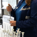 Auf dem Bild ist eine Labortechnikerin zu sehen, die in einem Labor arbeitet und mit einer Pipette Flüssigkeiten in Reagenzgläser füllt.