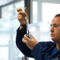 Auf dem Bild ist eine Person in einem Labor zu sehen, die mit Schutzbrille und Laborgeräten arbeitet, möglicherweise im Bereich Biochemie oder Chemie.