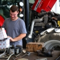Eine Person arbeitet als Land- und Baumaschinentechniker an einem landwirtschaftlichen Fahrzeug und überprüft Ersatzteile.