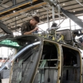 Auf dem Bild ist ein Luftfahrzeugtechniker zu sehen, der an einem Hubschrauber arbeitet und Wartungs- oder Reparaturarbeiten durchführt.