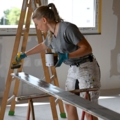 Eine Malerin streicht eine Holzleiste mit Farbe.