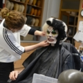 Eine Maskenbildnerin schminkt eine Person mit auffälligem Make-up in einer Werkstatt.