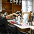 In dem Bild ist eine Schauspielerin in einem Maskenbildnerstudio zu sehen, die vor einem Spiegel sitzt.