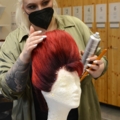 Eine Maskenbildnerin stylt eine rote Perücke auf einem Styroporkopf.