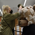 Eine Maskenbildnerin hilft dabei, einem/einer Schauspieler/in eine große Tiermaske aufzusetzen.