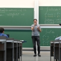 Ein Hochschullehrer für Mathematik steht in einem Klassenzimmer vor Tafeln mit mathematischen Formeln und unterrichtet.