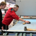 Zwei Medienfachmänner arbeiten an einer Druckmaschine, wobei eine Person den Druckvorgang kontrolliert.