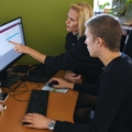 Zwei Medienfachleute arbeiten konzentriert an Computern und besprechen Informationen auf dem Bildschirm.