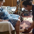 Das Bild zeigt eine Pflegekraft, die einer älteren Person beim Anziehen von Schuhen hilft.
