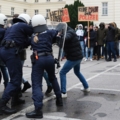 Das Bild zeigt Exekutivbedienstete im Polizeidienst in voller Ausrüstung, die bei einer Demonstration eine Menschenmenge zurückhalten.
