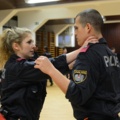 Auf dem Bild üben zwei Personen in Polizeiuniform Nahkampftechniken in einer Trainingseinrichtung.