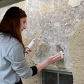 Auf dem Bild ist eine Person zu sehen, die eine Wand mit restauratorischen Techniken behandelt, um sie zu pflegen und zu erhalten.