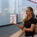 Eine Frau hält ein Schild in einem Flughafen, was auf einen Beruf im Bereich Reiseleitung hinweist.
