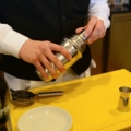 Eine Restaurantfachfrau bereitet mit einem Cocktailshaker und Barutensilien Getränke zu.