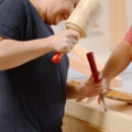 Eine Zimmerin arbeitet mit einem Holzhammer und einem Meißel an einem Holzstück.