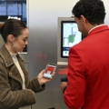 Eine Person in roter Uniform hilft einer anderen Person dabei, einen mobilen Boarding-Pass auf ihrem Handy zu scannen.