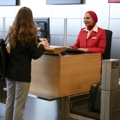 Eine Person in einer Uniform arbeitet am Check-in-Schalter eines Flughafens und hilft einem Reisenden.
