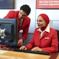 Auf dem Bild sind zwei Personen in roter Berufskleidung an einem Empfangsschalter zu sehen, die am Flughafen im Kundenservice arbeiten.