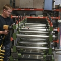Ein Mann arbeitet in einer Werkstatt mit einer Maschine, die mehrere Metallrollen verarbeitet.