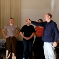 Auf dem Bild ist eine Gruppe von Menschen zu sehen, die an einer Schauspielprobe oder einem Schauspielworkshop teilzunehmen, wobei eine Person Anweisungen gibt oder eine Szene inszeniert.
