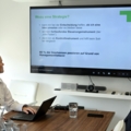 Das Bild zeigt zwei Personen in einem Meeting, die eine Präsentation über strategische Unternehmensentscheidungen betrachten.