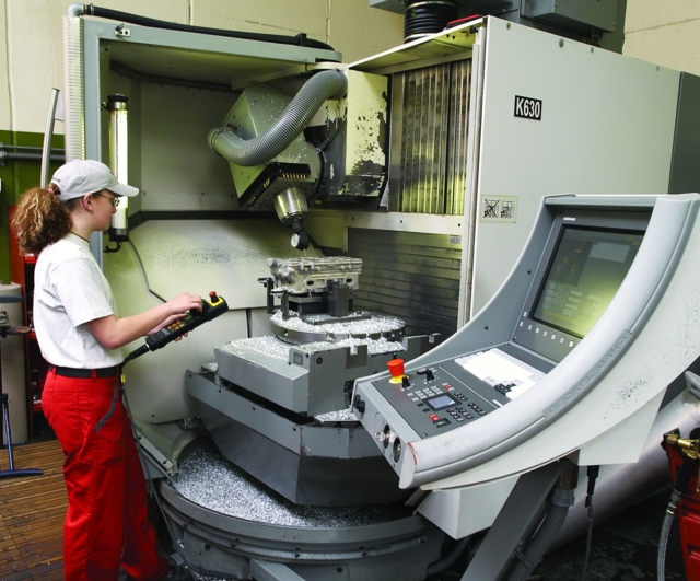 Eine Person bedient eine CNC-Fräsmaschine in einem industriellen Umfeld.