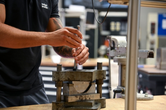 Eine Person arbeitet an einer Metallpresse in einer Werkstattumgebung.