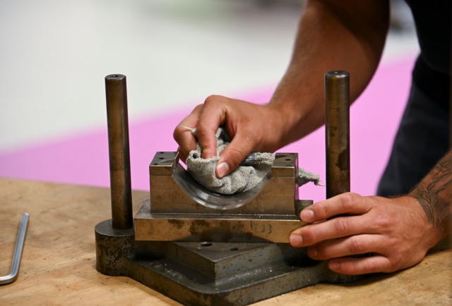 Auf dem Bild ist zu sehen, wie jemand mit einem Tuch ein Metallteil in einer Werkstatt reinigt oder bearbeitet.