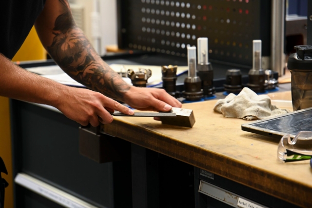 Die Person auf dem Bild arbeitet in einer Werkstatt und verwendet ein Werkzeug auf einer Werkbank.