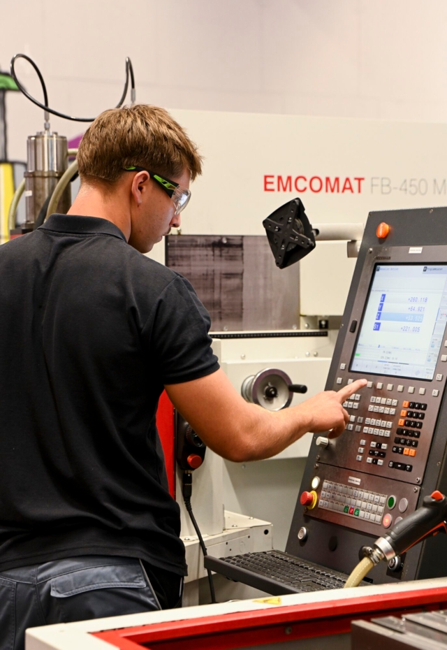 Eine Person bedient eine CNC-Maschine in einem industriellen Umfeld.