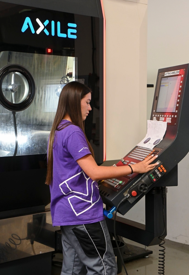Eine Person bedient eine CNC-Maschine in einem technischen oder industriellen Umfeld.