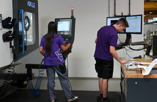 Zwei Personen bedienen Maschinen in einer Werkstatt.