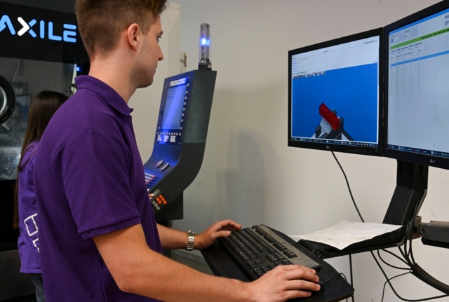 Die Person auf dem Bild arbeitet an einem Computerarbeitsplatz und überwacht oder steuert möglicherweise eine CNC-Maschine.