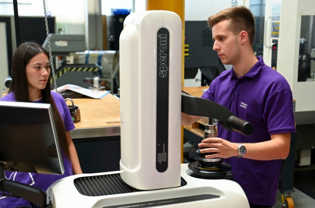 Das Bild zeigt zwei Personen, die mit einer Präzisionsmaschine arbeiten.